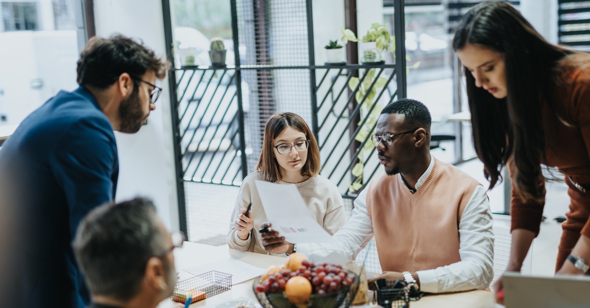 A diverse team gathers around a table in a bright office, reviewing notes during a collaborative meeting.